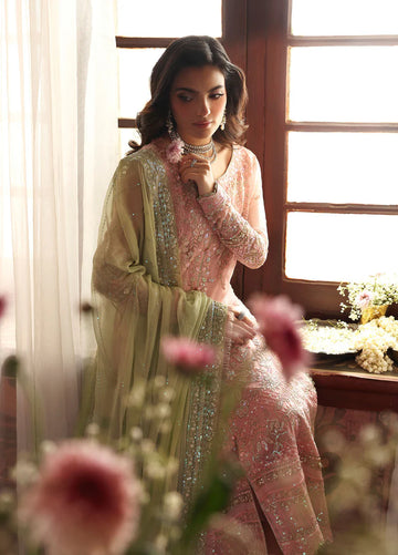 Woman in a traditional outfit with floral decorations, sitting by a window with flowers in the foreground.