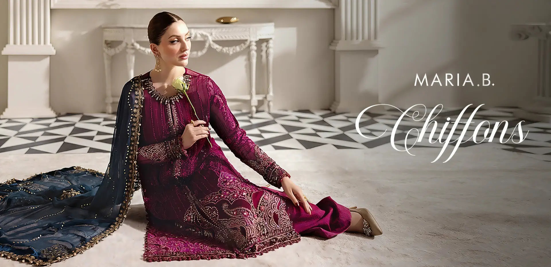 Woman in a purple embroidered dress sitting on a rug in a decorative room with 'Maria B. Chiffons' branding.