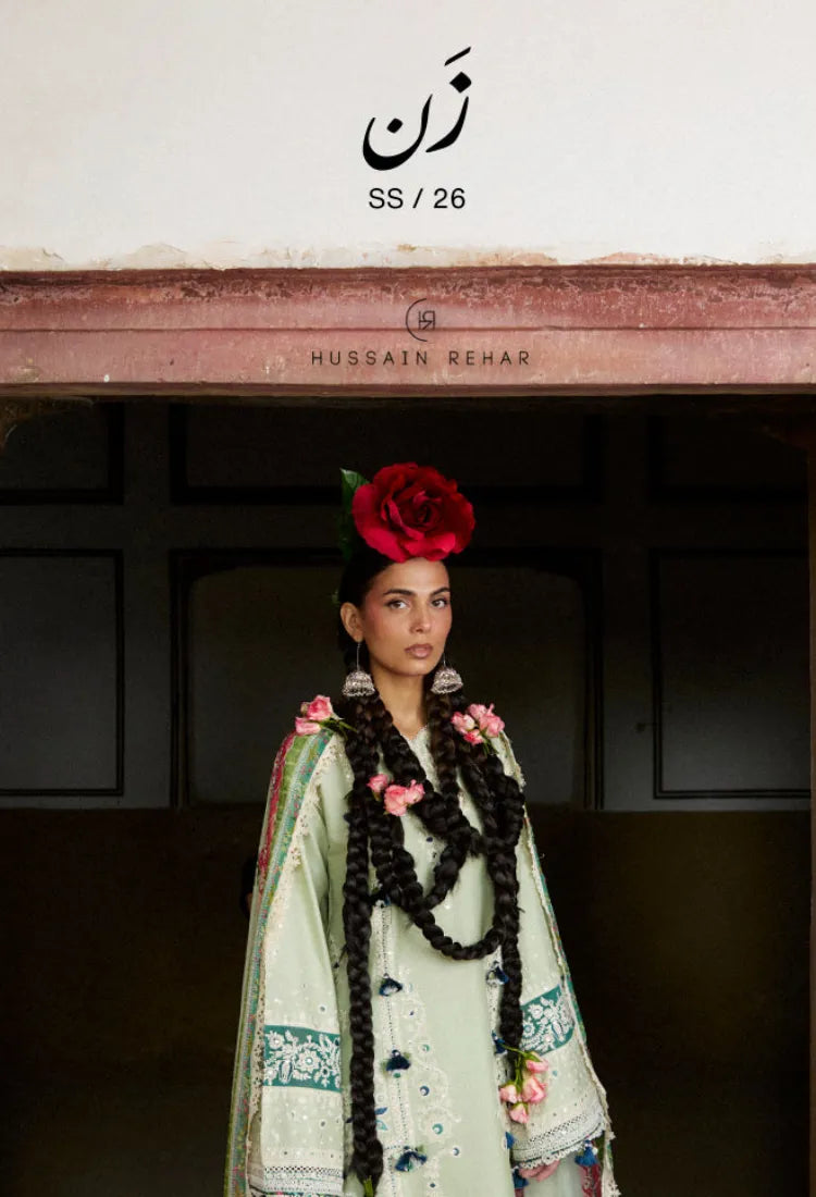 Woman in traditional attire with floral decorations, standing in front of a stone wall.